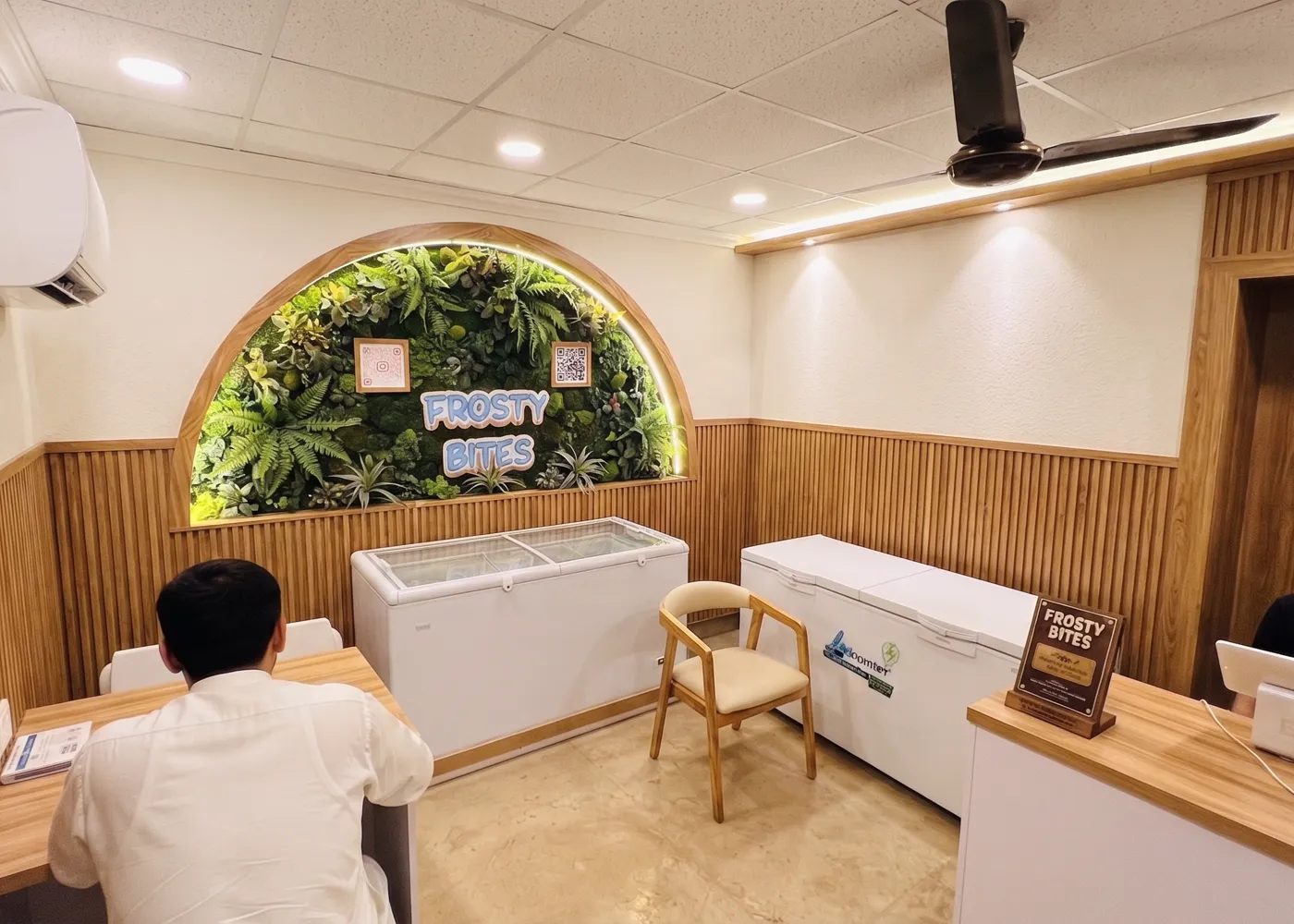 Inside the Frosty Bites shop in Bahawalpur — wood panelling, a living plant wall and the FROSTY BITES sign above the freezers